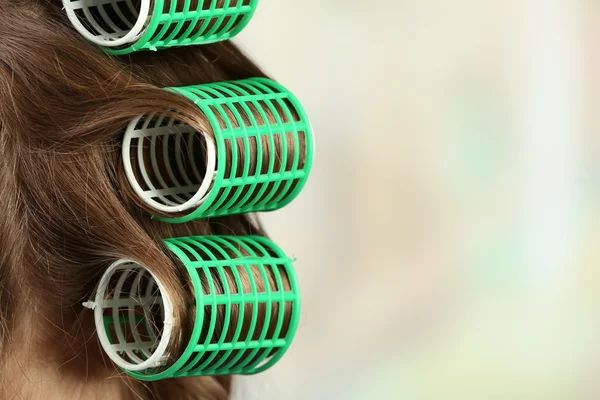 Long female hair during hair dressing with curler, close-up, on light background