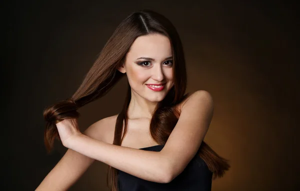 Beautiful young woman with long hair on dark brown background — Stock Photo, Image