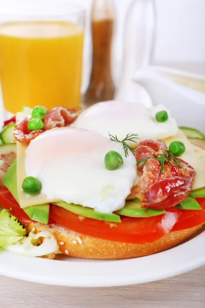 Sandwich with poached eggs, bacon and vegetables on plate on wooden background — Stock Photo, Image