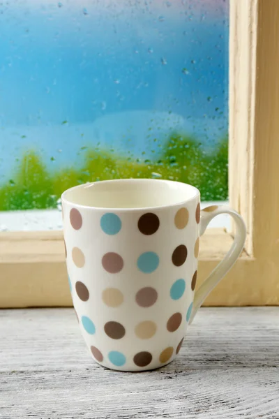 Cup of hot drink on windowsill on rain background — Stock Photo, Image