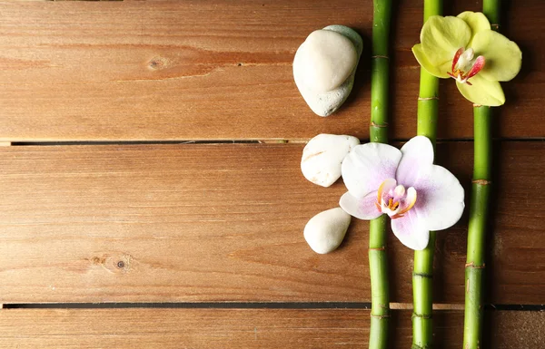 Flores de orquídea y bambú con piedras de pila sobre fondo de madera — Foto de Stock