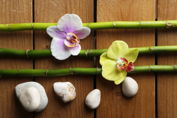 Bunga anggrek dan bambu dengan tumpukan batu di latar belakang kayu — Stok Foto