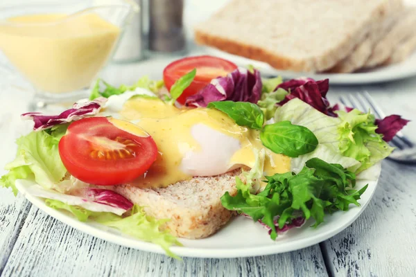 Toast with egg Benedict and tomato on plate on wooden table — Stock Photo, Image