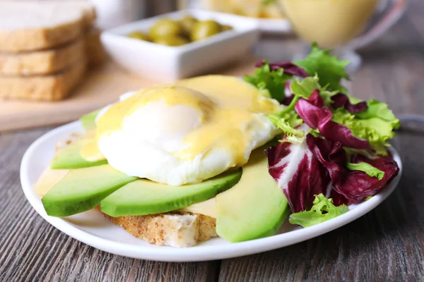 Toast with egg Benedict and avocado on plate on wooden table — Stock Photo, Image