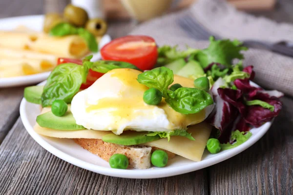 Toast with egg Benedict and avocado on plate on wooden table — Stock Photo, Image