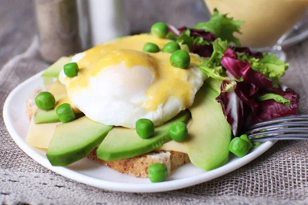 Roti panggang dengan telur Benedict dan alpukat di piring di atas meja tutup — Stok Foto