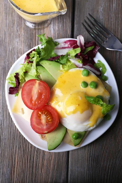 Toast with egg Benedict and avocado on plate on wooden table — Stock Photo, Image