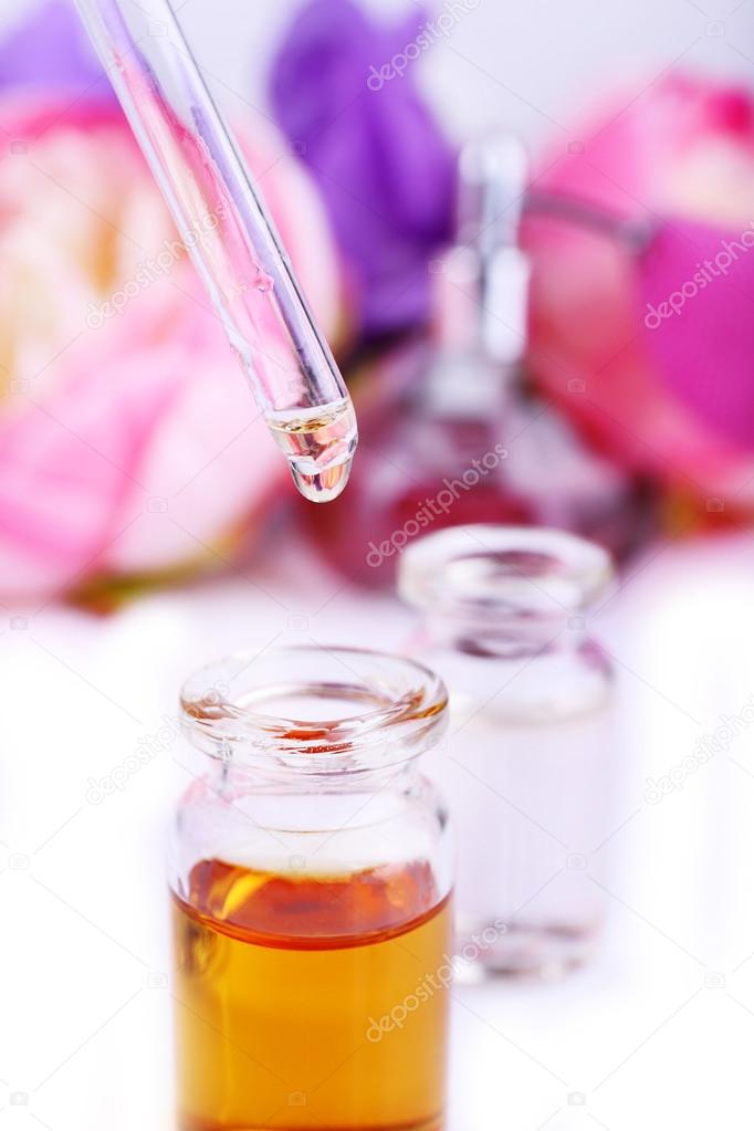 Dropper bottle of perfume with flowers on light background