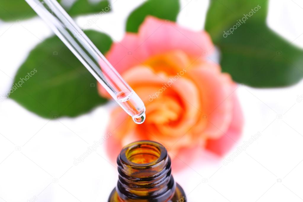 Dropper bottle of perfume with rose on light background