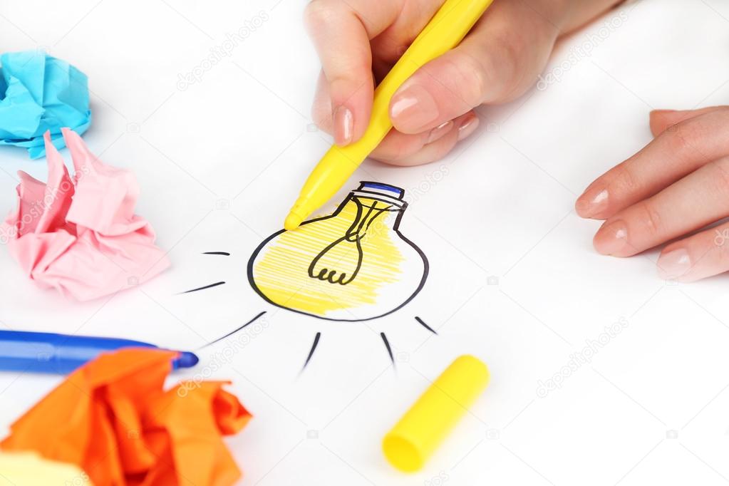 Female hand drawing symbol of idea as light bulb on sheet of paper, on white background