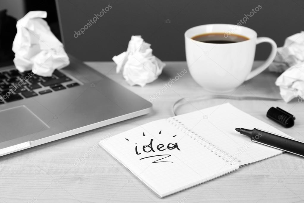 Cup of coffee with crumpled paper and note Idea in notebook on wooden table and dark background