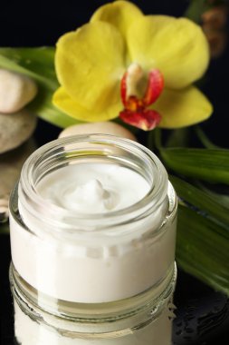 Koyu arka plan üzerinde orkide çiçek ile yüz kremi