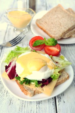 Yumurta Benedict ile tost ve ahşap masa üzerinde tabakta domates