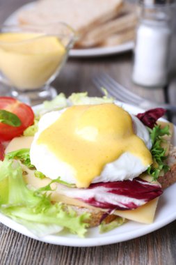 Yumurta Benedict ile tost ve ahşap masa üzerinde tabakta domates