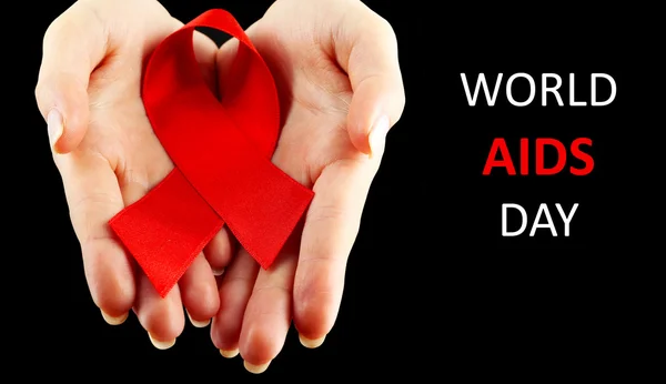 Red AIDS ribbon in female hands on black background — Stock Photo, Image