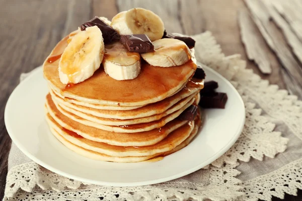 Stapel van heerlijke pannenkoeken met chocolade, honing en segmenten van banaan op plaat en servet op houten tafel achtergrond — Stockfoto