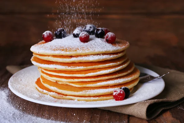 Bunt med läckra pannkakor med strösocker och bär på tallrik och servett på trä bakgrund — Stockfoto