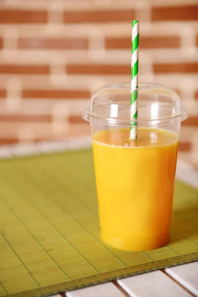 Jugo de naranja en taza cerrada de comida rápida con tubo en mesa de madera y fondo de pared de ladrillo —  Fotos de Stock