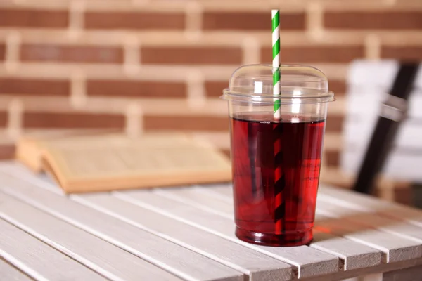 Pomegranate juice in fast food closed cup with tube and book on wooden table and brick wall background