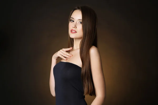 Όμορφη νεαρή γυναίκα με μακριά μαλλιά σε σκούρο καφέ φόντο — Φωτογραφία Αρχείου