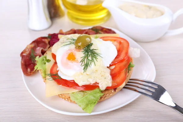 Sandwich with poached egg, tomato and bacon on plate on wooden background — Stock Photo, Image