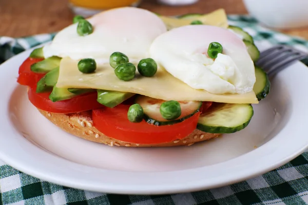 Sandwich with poached eggs, cheese and vegetables on plate on table close up — Stock Photo, Image