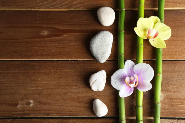 Квіти орхідей і бамбук з купами каменів на дерев'яному фоні — стокове фото
