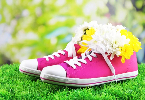 Hermosos zapatos de goma con flores en el interior sobre hierba verde, sobre fondo brillante — Foto de Stock