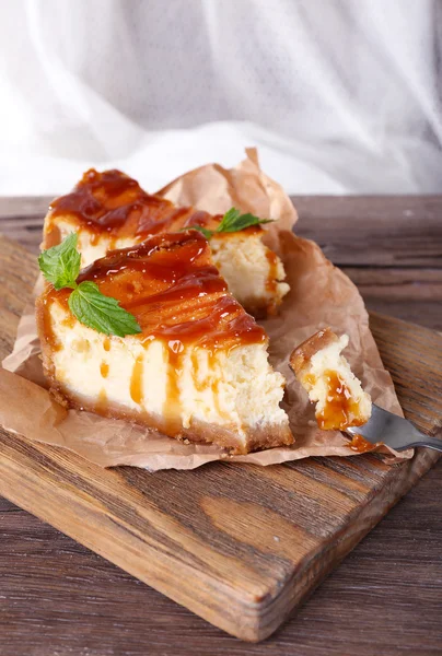 Cheese cake on piece of paper on cutting board on wooden table on curtain background — Stock Photo, Image