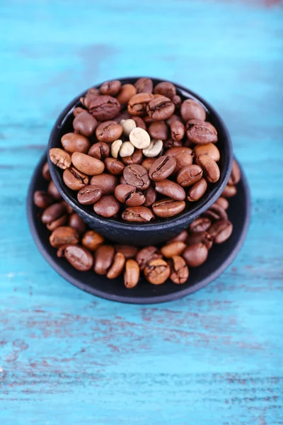 Coffee beans in black ceramic cup on blue wooden background — Stock Photo, Image