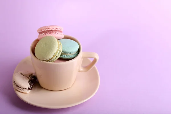 Assortment of gentle colorful macaroons in colorful mug on color background — Stock Photo, Image