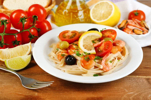 Välsmakande pasta med räkor, musslor, svarta oliver och tomatsås på plattan på trä bakgrund — Stockfoto