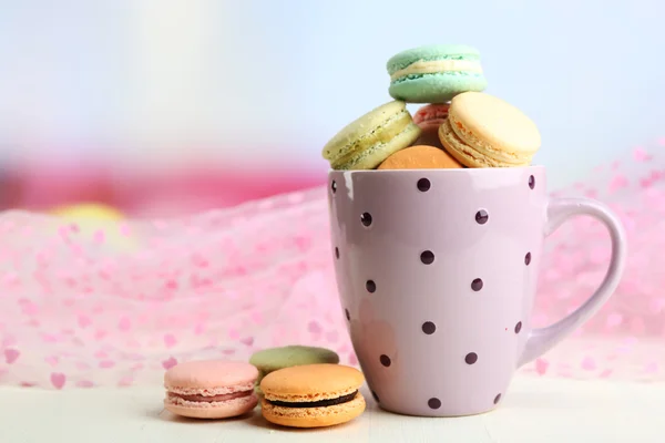 Assortment of gentle colorful macaroons in colorful mug on color wooden table, on light background — Stock Photo, Image