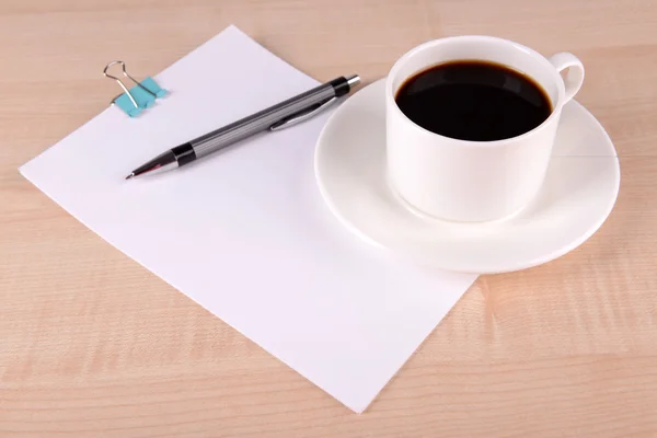 Kopp kaffe på fat med ark av papper och penna på träbord bakgrund — Stockfoto