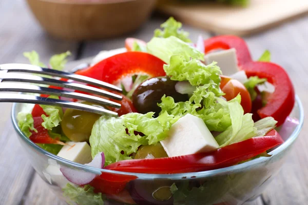 Greek salad in glass dish with fork on wooden table background — Stock Photo, Image