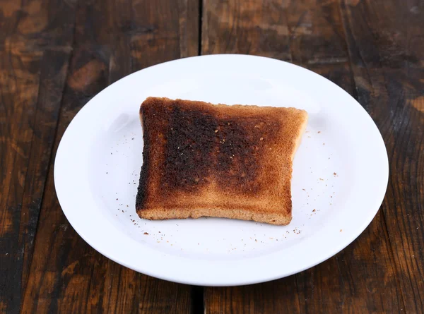 Burnt toast bread on plate, on wooden table background — Stock Photo, Image