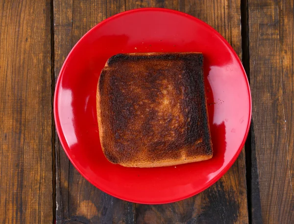 Burnt toast bread on red plate, on wooden table background — Stock Photo, Image