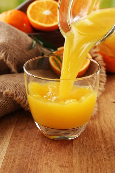 Pouring orange juice from glass carafe, on wooden table background — Stock Photo, Image