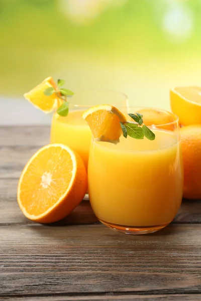 Glass of orange juice and slices on wooden table and bright background — Stock Photo, Image