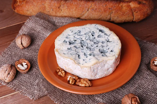 Blue cheese on earthenware dish with nuts and baguette on burlap cloth and wooden table background — Stock Photo, Image