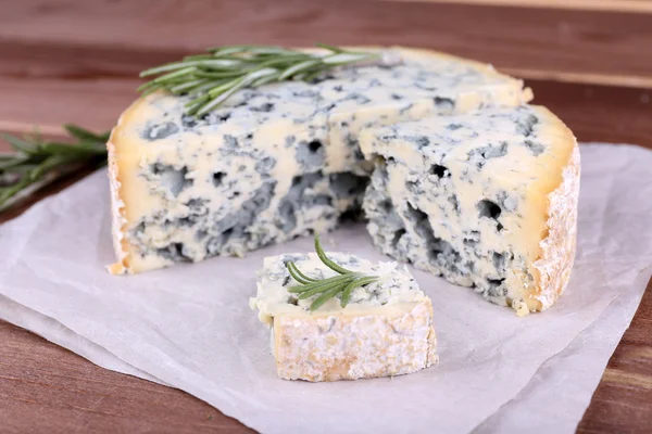 Blue cheese with sprigs of rosemary on sheets of paper and wooden table background — Stock Photo, Image