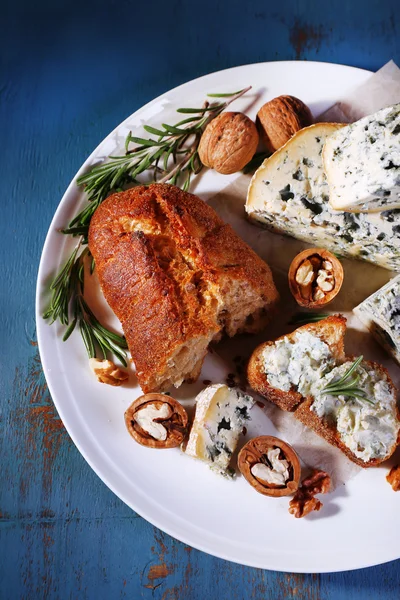 蓝纹奶酪与小枝迷迭香、 面包和板和彩色木桌背景上的螺母 — 图库照片
