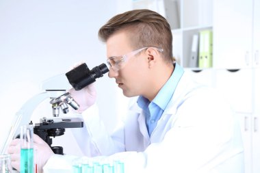 Erkek bilim adamı laboratuvarda mikroskop kullanıyor.