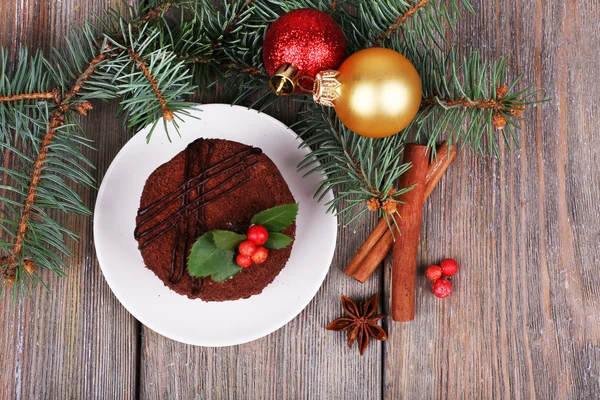 Delicious chocolate cake on saucer with holly and berry on Christmas decoration and wooden background — Stock Photo, Image