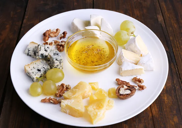 Diferentes tipos de queijo com uva, nozes e pires no prato em fundo de mesa de madeira — Fotografia de Stock