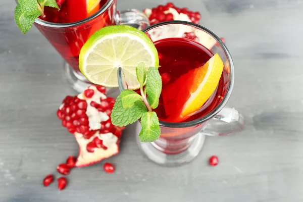 Pomegranate drink in glasses with mint and slices of orange and lime on color wooden background — Stock Photo, Image