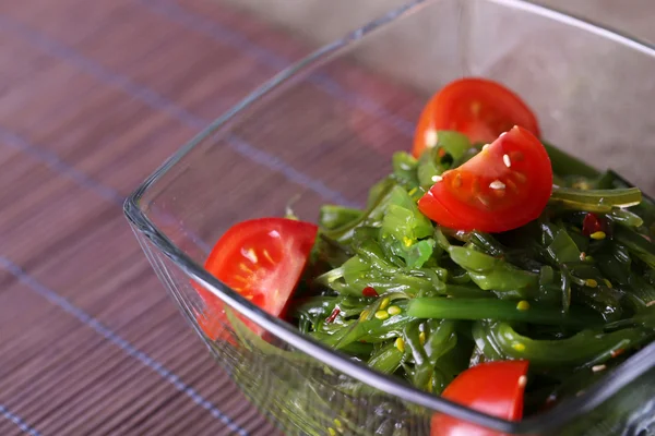 Salade d'algues avec tranches de tomate cerise dans un bol en verre sur un tapis de bambou et toile de jute — Photo