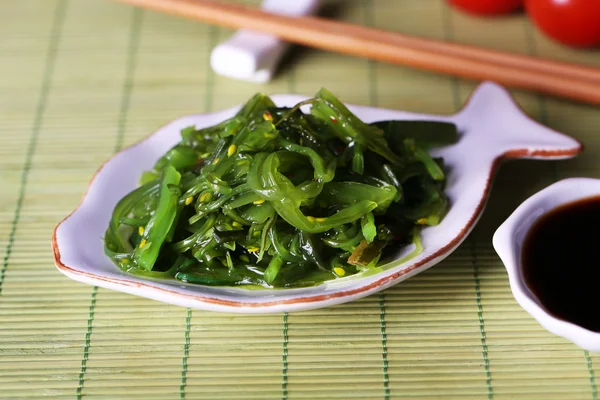 Salade d'algues dans une assiette sur fond de tapis de bambou — Photo