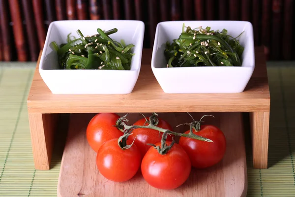 Salada de algas marinhas com tomates cereja em suporte de madeira e bambu no fundo — Fotografia de Stock