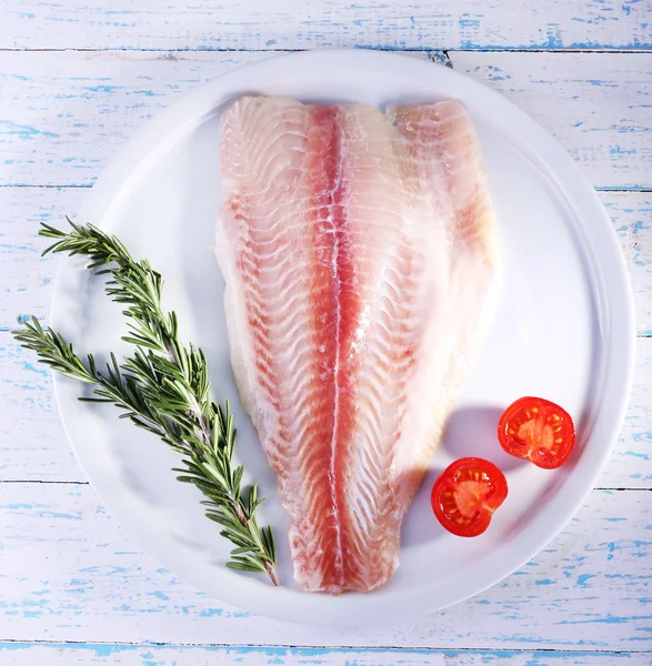 Pangasius fillet with herb and sliced cherry tomatoes on plate and color wooden table background — Stock Photo, Image